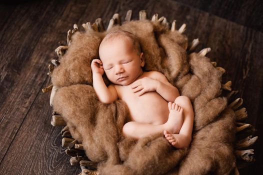 Newborn baby boy is napping in a wooden basket at a newborn photoshoot. High quality photo