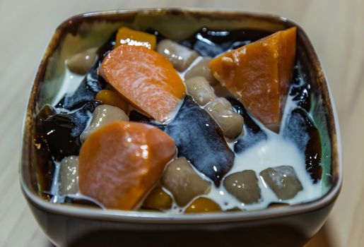 Traditional taiwanese iced dessert with Grass jelly, Taro balls, Tofu pudding, Sweet potato balls and Boba Topping with Fresh milk in Earthenware bowl. No focus, specifically.