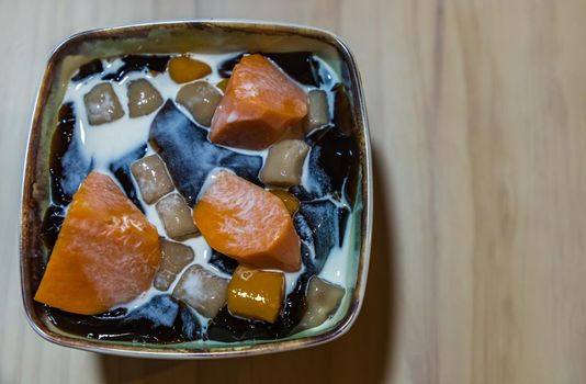 Traditional taiwanese iced dessert with Grass jelly, Taro balls, Tofu pudding, Sweet potato balls and Boba Topping with Fresh milk in Earthenware bowl. No focus, specifically.