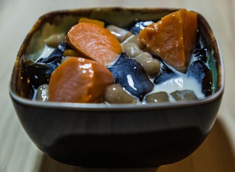 Traditional taiwanese iced dessert with Grass jelly, Taro balls, Tofu pudding, Sweet potato balls and Boba Topping with Fresh milk in Earthenware bowl. No focus, specifically.
