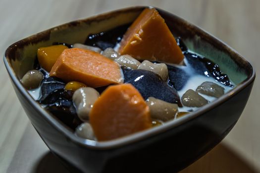 Traditional taiwanese iced dessert with Grass jelly, Taro balls, Tofu pudding, Sweet potato balls and Boba Topping with Fresh milk in Earthenware bowl. No focus, specifically.