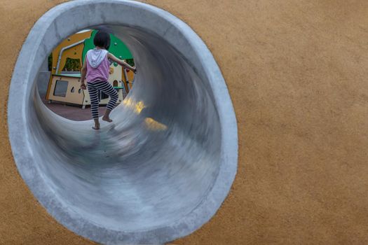 Bangkok, Thailand - Jul 25, 2020 : Asian little girl playing inside a tunnel in the park for children. Playground on background. Selective focus.