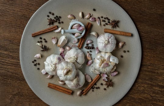 Garlic bulbs and Garlic cloves with Herbs spices, Cinnamon, Star anise and Pepper grain in Ceramic plate on Wooden rustic table. Copy space Concept of healthy food. Top view, Selective focus.