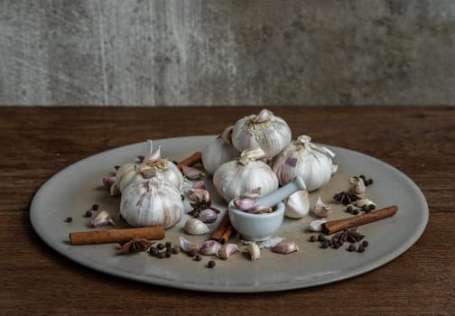 Garlic bulbs and Garlic cloves with Herbs spices, Cinnamon, Star anise and Pepper grain in Ceramic plate on Wooden rustic table. Copy space Concept of healthy food. Selective focus.