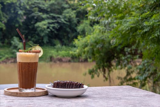 Honey lemon coffee with Chocolate Brownie Cake on wooden background with river view. Refreshing summer food and drink  concept. Selective focus.