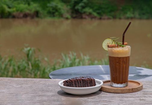 Honey lemon coffee with Chocolate Brownie Cake on wooden background with river view. Refreshing summer food and drink  concept. Selective focus.