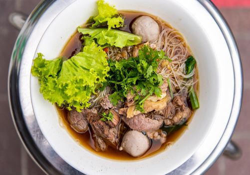 Thai beef clear soup white rice noodle vermicelli with braised beef, meatball and vegetable. Delicious street fast food in Thailand. Top view, Selective focus.