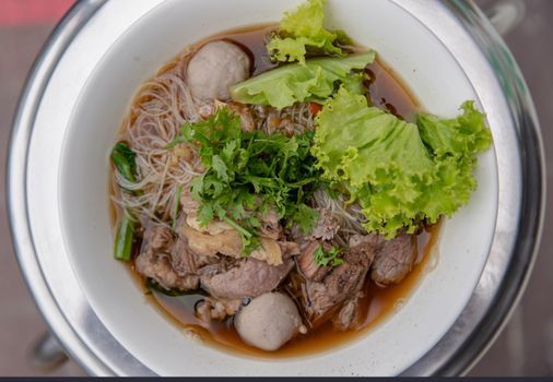 Thai beef clear soup white rice noodle vermicelli with braised beef, meatball and vegetable. Delicious street fast food in Thailand. Top view, Selective focus.