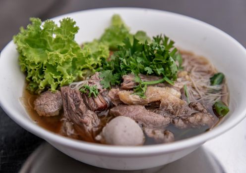 Thai beef clear soup white rice noodle vermicelli with braised beef, meatball and vegetable. Delicious street fast food in Thailand. Oblique view from the top, No focus, No focus, specifically.