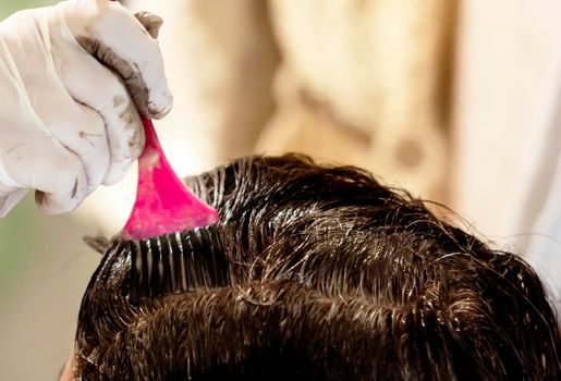 a young brunette caucasian woman dying her hair with a pink brush using white gloves at her home. Detail on the brush