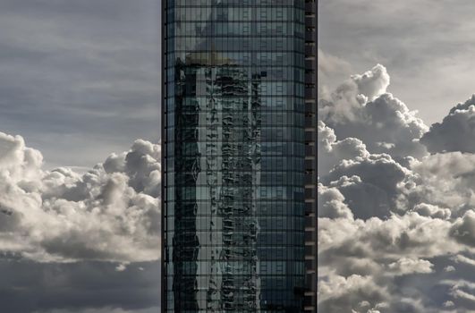 Bangkok, Thailand - Sep 24, 2020 : Angular geometric mirror cladding on a modern building with repeating structure and reflected sky and clouds. No focus, specifically.