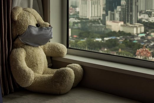 Sad teddy bear in protective medical masks sits on windowsill and looks out window. Stay at home quarantine coronavirus pandemic prevention, Virus outbreak in a world. No focus, specifically.
