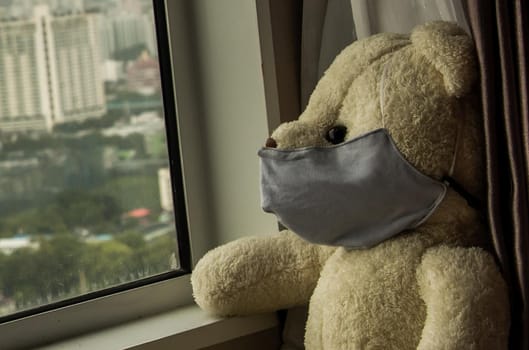 Close-up of Sad teddy bear in protective medical masks sits on windowsill and looks out window. Stay at home quarantine coronavirus pandemic prevention, Virus outbreak in a world. No focus, specifically.