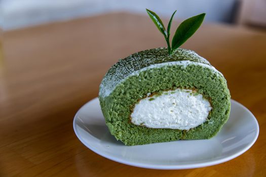 Matcha green tea roll cake and Decor with Tea leaf on White plate on wooden table. Sweet or dessert, Focus and blur.