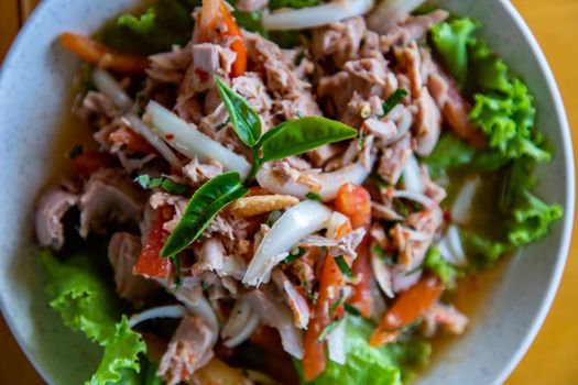 Close- up of Spicy tuna salad and Decor with Tea leaf on White plate on wooden table. Homemade thai style, Focus and blur.