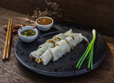 Thai fresh spring rolls served with Sweet sauce and Spring onions on black plate. Selective focus.