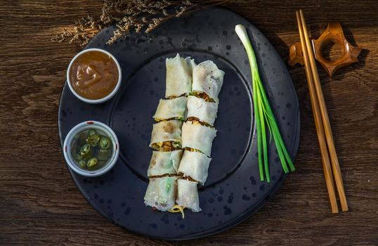Thai fresh spring rolls served with Sweet sauce and Spring onions on black plate. Selective focus.