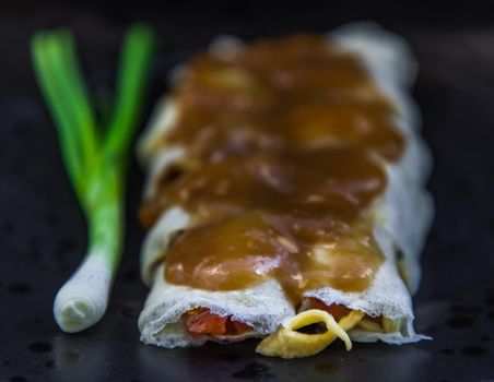 Close-up of Thai fresh spring rolls Topped with Sweet sauce with Spring onions on black plate. Selective focus.