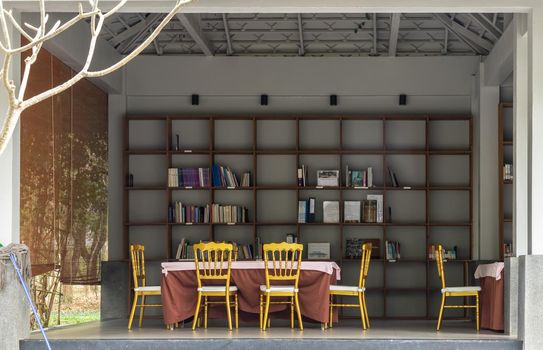 Phetchaburi, Thailand - Feb 29, 2020 : Shelf with boxes and books. Wooden table and wooden chairs in open view relaxing room by the garden. No focus, specifically.