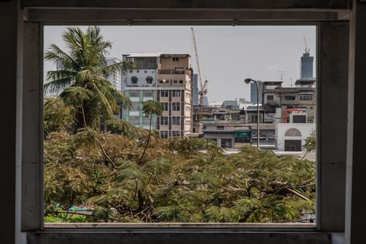 View of buildings and big trees in Bangkok. Looks through the window frames in abandoned building. Selective focus.