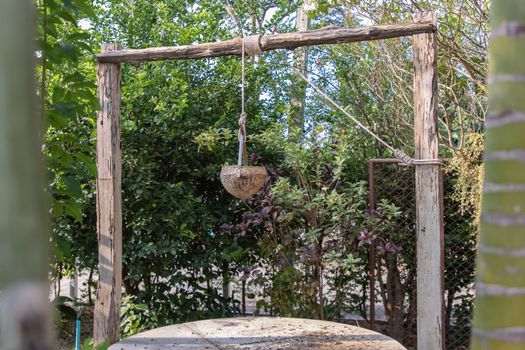 Old wooden well (water source) in traditional village folk style. At time of scooping the rope, put wooden water scoop into the pond to draw water.