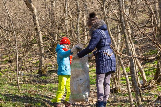 A girl collects garbage in the forest, a girl holds a large garbage bag