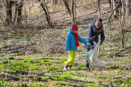 A girl and a woman collect garbage at the forest edge