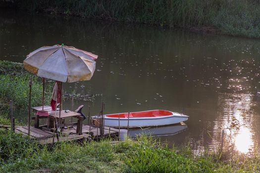 Rowboat moored to a rustic jetty along the canal amongst grass and water in a scenic rural landscape. Selective focus.