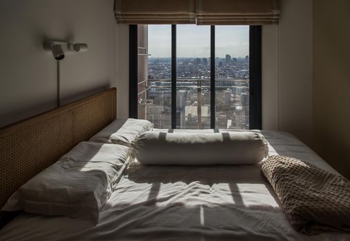 Interior white bedroom with brown curtains and white pillows, blanket on wooden bed classic illuminated by sunlight in the morning. For rest and sleep. Minimalist style bedroom. Selective focus.