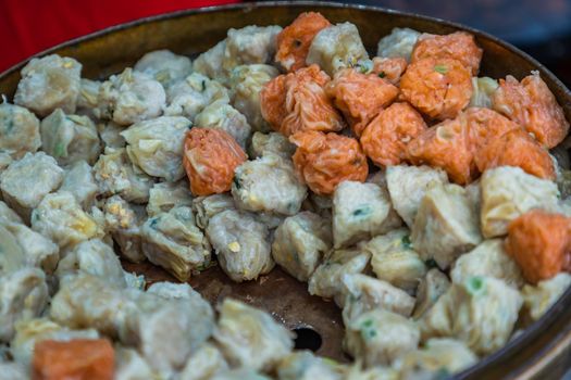 Close-up of Shumai (Shaomai) or Kanom Jeeb' a 'Dim Sum' Chinese traditional steamed dumplings food with shrimp and pork inside in metal tray for sale at street market. Traditional breakfast asian styles. Selective focus.