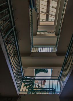 Bangkok, Thailand - 25 Jan 2020 : Looking up from under view upstairs walkway of an old apartment building with green metal rails and skylight. Selective focus.