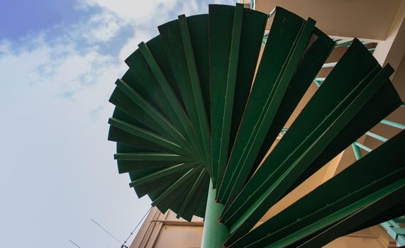 Green spiral staircase pattern view from below. Spiral stairs circle in courtyard architecture. Outdoor ladder decoration interior. Copy space, Selective focus.