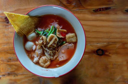 Yentafo Thai Noodle with pink soup in ceramic bowl on wooden table. Top view, Copy space, Selective focus.