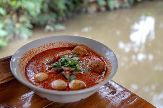 Spicy tom yum pork soup or Spicy lemongrass flavored soup with fish balls in ceramic bowl on wooden table. Copy space, Selective focus.