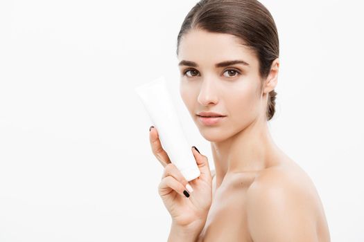 Beauty Youth Skin Care Concept - Beautiful Caucasian Woman Face Portrait holding and presenting cream tube product. Beautiful Spa model Girl with Perfect Fresh Clean Skin over white background