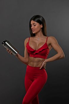 brunette girl in red leggings and a top on a gray background with a shaker in her hands