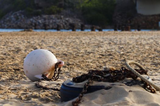 White mooring buoy tied to a rusty chain and weight on coastal river sandbank, Mossel Bay, South Africa