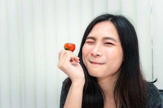 Asian pretty woman holding and eating fresh strawberry is red berry fruit color and sweet juicy with enjoy and happy emotion in concept food, healthy eating in life
