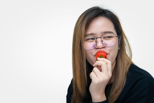 Asian pretty woman holding and eating fresh strawberry is red berry fruit color and sweet juicy with enjoy and happy emotion in concept food, healthy eating in life