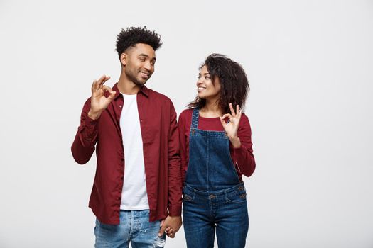 Portrait of a cheerful young african couple standing together and showing ok gesture isolated over white background.