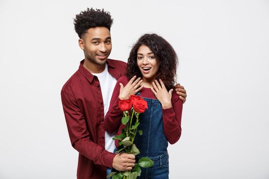 Beautiful elegant couple is hugging and smiling, on gray background. Girl is holding roses.