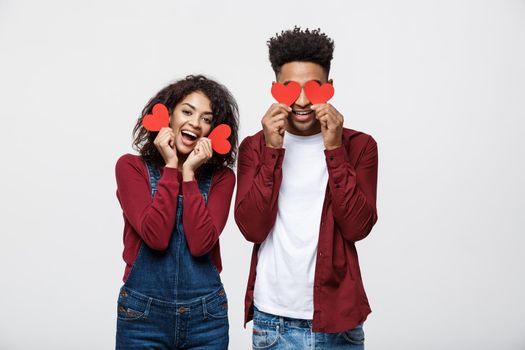 Beautiful Afro American couple holding two red paper heart, looking at camera and smiling, isolated on white background.