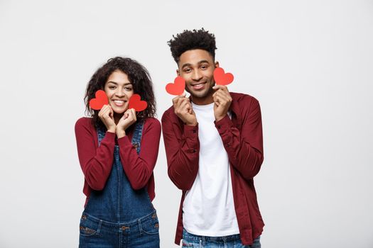 Beautiful Afro American couple holding two red paper heart, looking at camera and smiling, isolated on white background.