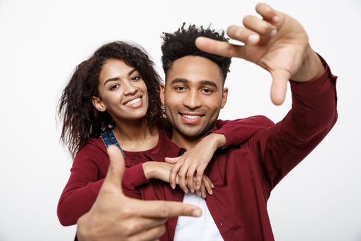 Happy young African American couple looking through a finger frame and smiling while standing isolated on white