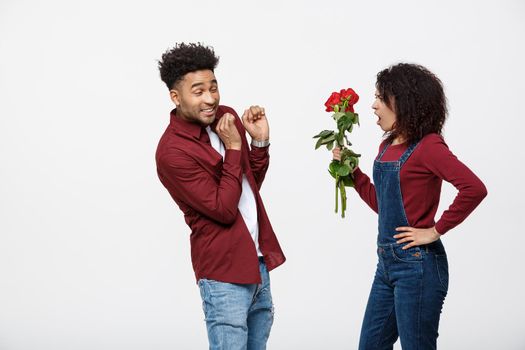 Portrait of a disappointed young woman holding red rose with while standing and angry on her boyfriend isolated over white background.