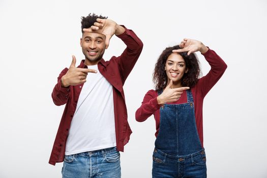 Happy young African American couple looking through a finger frame and smiling while standing isolated on white