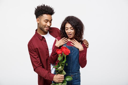 Beautiful elegant couple is hugging and smiling, on gray background. Girl is holding roses.