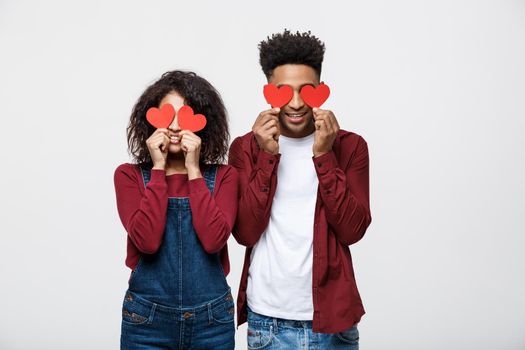 Beautiful Afro African American couple is holding red paper hearts and smiling, on gray background.