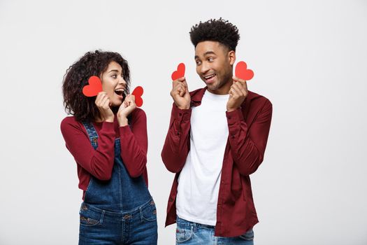 Beautiful Afro American couple holding two red paper heart, looking at camera and smiling, isolated on white background.