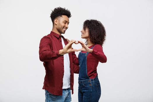 Portrait of a smiling young african couple dressed in casual clothes hugging and showing heart gesture with fingers isolated over white background.